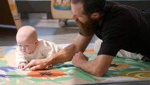 Homme jouant avec un bébé sur un tapis contenant divers formes géométriques de couleur